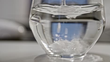 Dropping-effervescent-tablet-into-water-in-ultra-slow-motion,-office-background