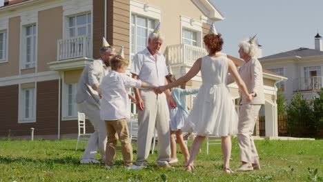 family dancing and celebrating birthday of grandfather outdoors