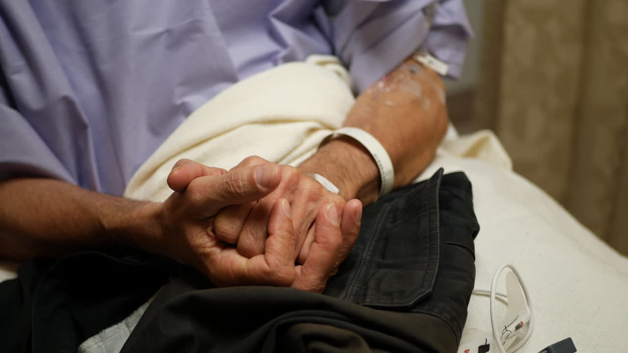 A middle aged male medical patient sits in a hospital bed rubbing his hands together nervously while waiting to go into his surgery