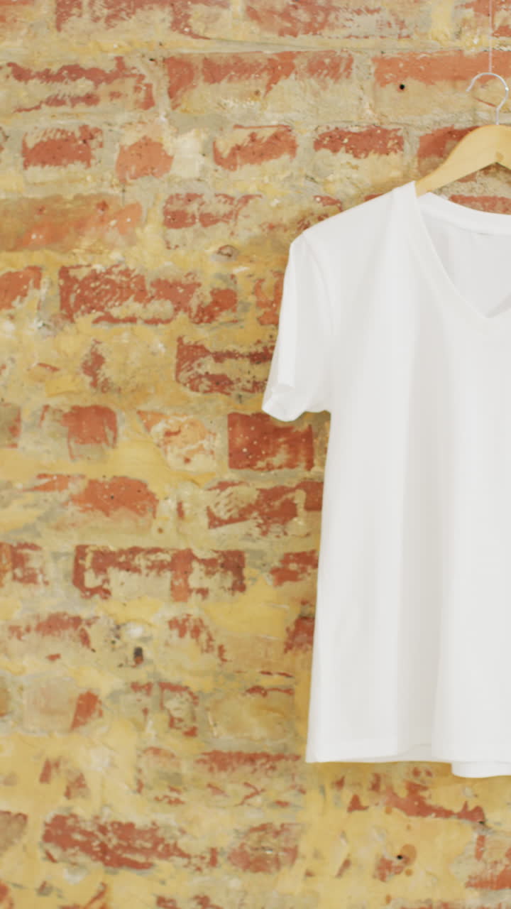 Vertical video of close up of white t shirt hanging on brick wall background with copy space