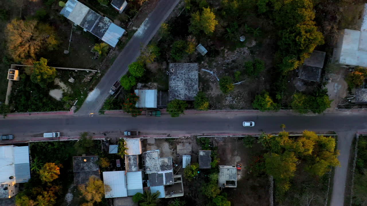 Drone shot downward angle of white car driving through the city of Merida Mexico