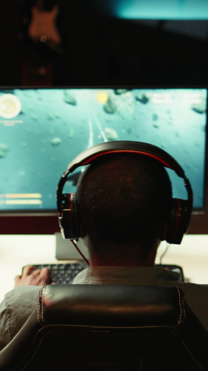 Video verticale. Un uomo gioca a un videogioco ambientato nello spazio sul PC, mentre indossa le cuffie
