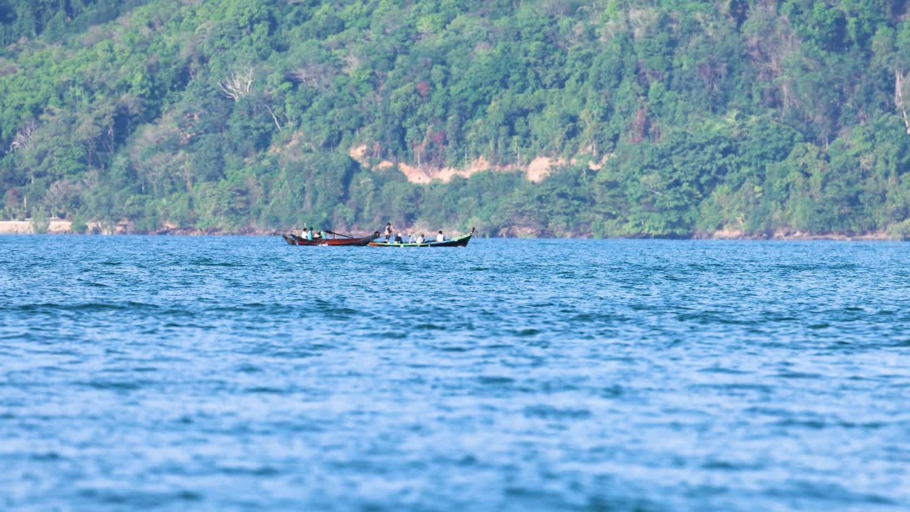 태국 푸켓 근처의 평온한 바다를 가로질러 달리는 긴 리 보트, 밝은 낮빛 아래 잔잔한 녹색 언덕을 배경으로
