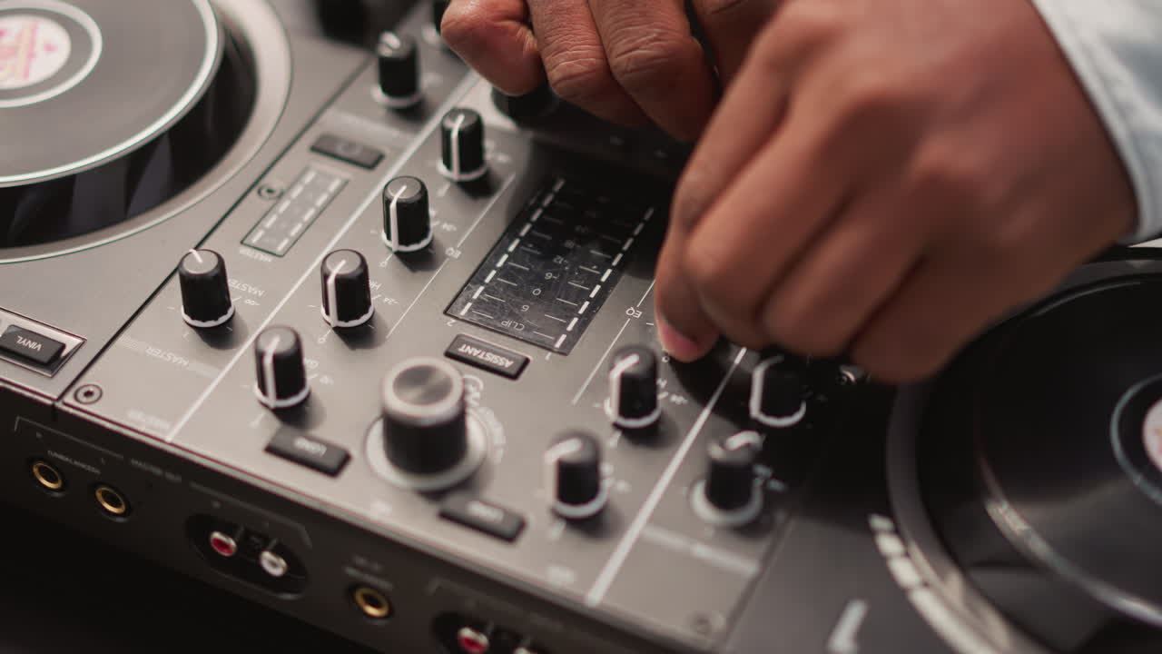 Mains ajustant les boutons du mixeur sur le contrôleur pendant un set DJ de rue en direct, gros plan sur la platine et le fader, éclairage ambiant chaud, mouvements tactiles des doigts, technique précise de beatmatching et de scratch, urbain.