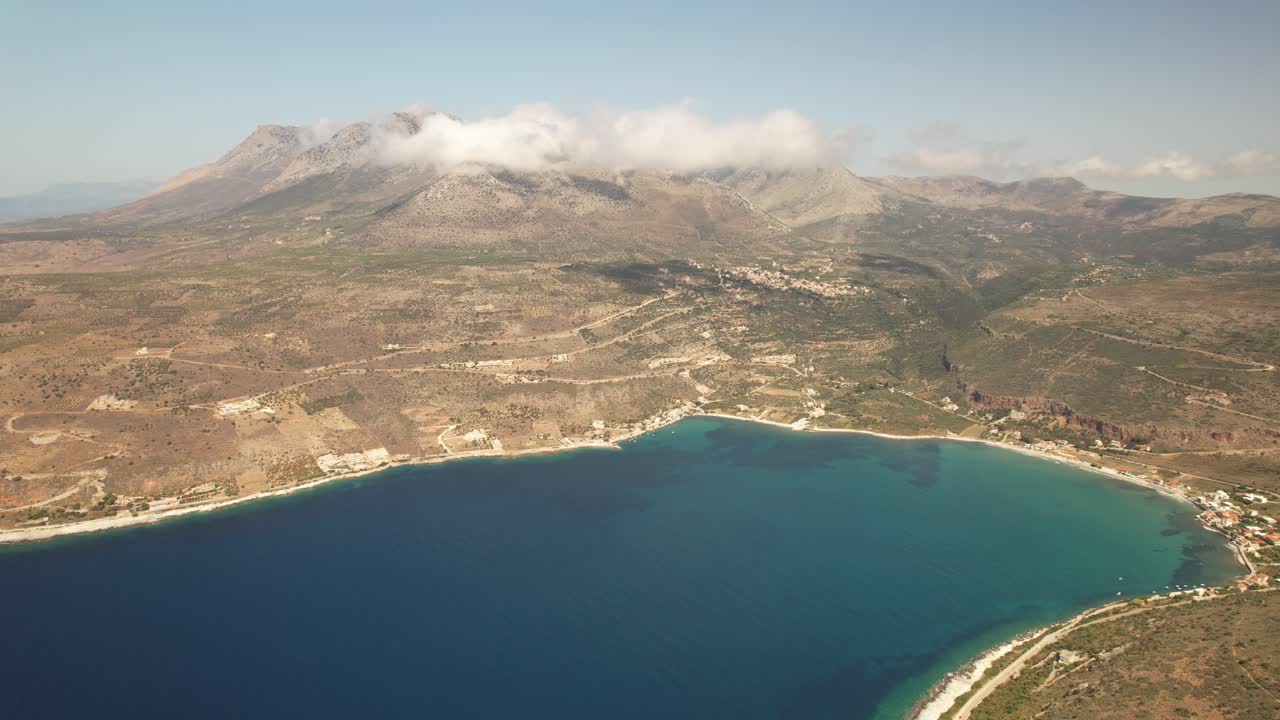 un dron vuela lentamente a gran altura junto al mar azul mientras las montañas están cubiertas de nubes en un caluroso día de verano en grecia