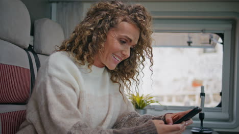 cheerful lady watching social media at cellphone in camper van close up.