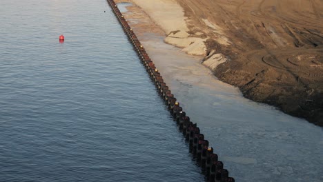 high-angle shot of a canal land expansion project, featuring steel sheet piling along the water and newly reclaimed terrain for future development