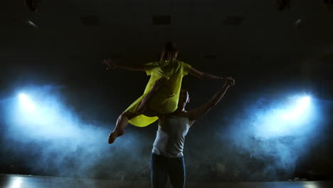 two dancers a man and a woman run to each other and a male partner raises a woman in a yellow dress in her arms and rotates in the air performing top support.