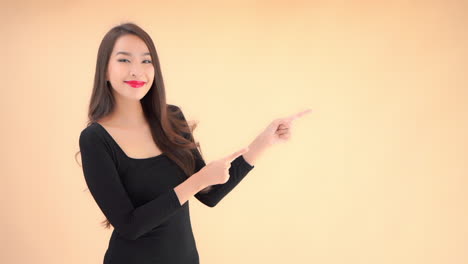 an attractive young woman in a little black dress raises her hands and points to an open space on the background