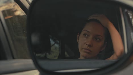 woman looking pensively in car mirror