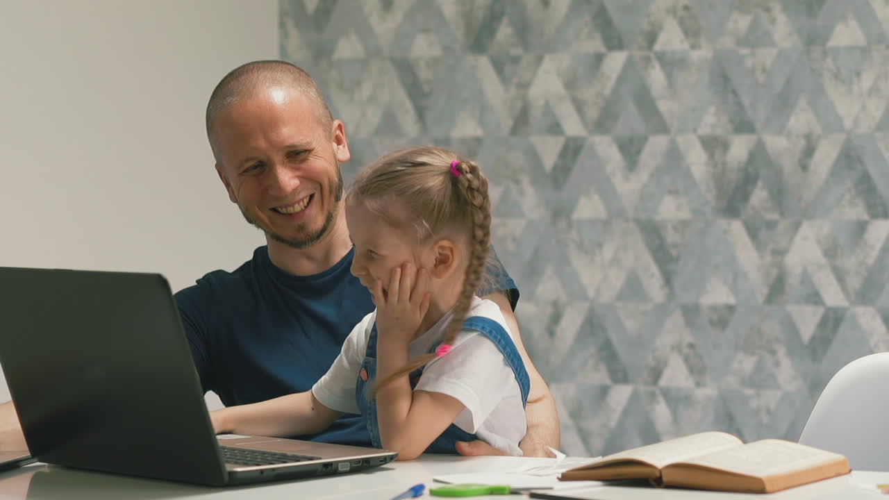 papá con la niña hace la tarea en la computadora portátil riendo en la mesa