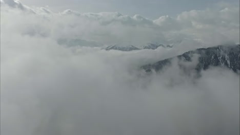 an idyllic aerial vista unfolds, showcasing a mountain range veiled beneath a low layer of clouds, with snow-capped peaks piercing through the mist