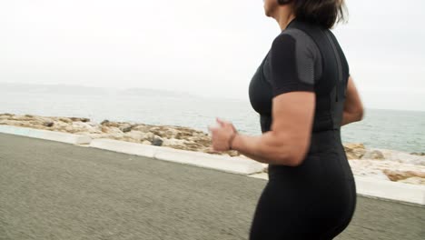 female athlete in sunglasses jogging along seaside road