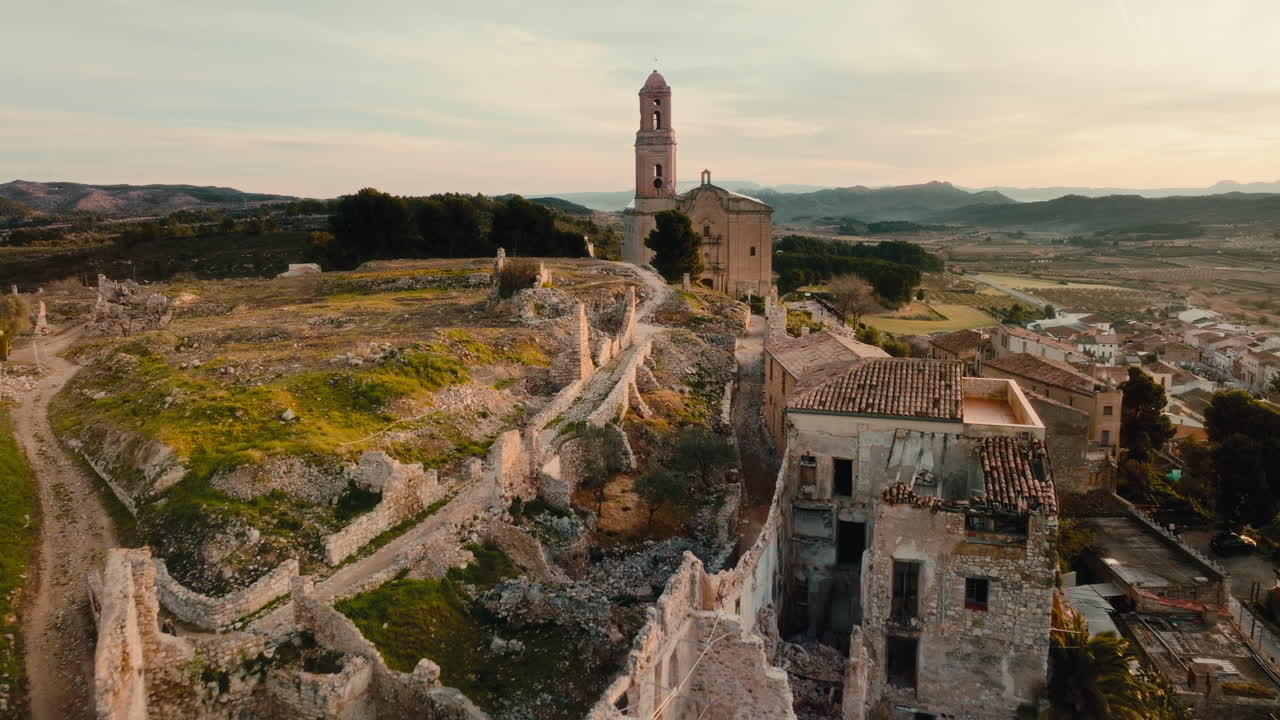Cinematic 4K aerial drone slow push in toward setting sun over an abandoned town Corbera d'ebre Spain, deserted after the Spanish Civil War. Golden hour light, historic church, dramatic landscape