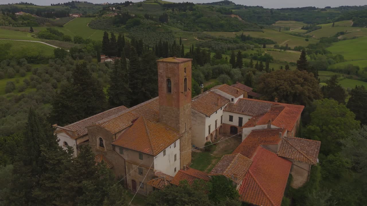 Drone flight over an old historic building in Tuscany, surrounded by rolling hills and vineyards. Beautiful rustic architecture and green countryside captured in soft daylight.