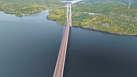 Sobrevolando-El-Puente-De-Metal-Y-Hormigón-De-Hogakustenbron-Con-Un-Bosque-Otoñal-Como-Telón-De-Fondo-En-Suecia