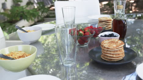 a breakfast spread features pancakes, strawberries, blueberries, and cereal on an outdoor table