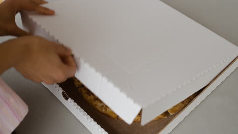 opening a pizza box to reveal the pizza inside