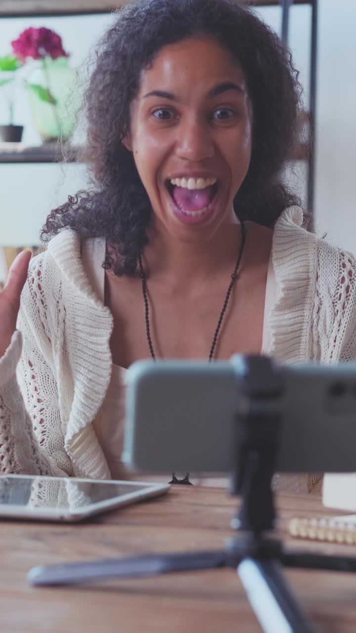Young african american woman blogger shoots video with phone camera sits at desk