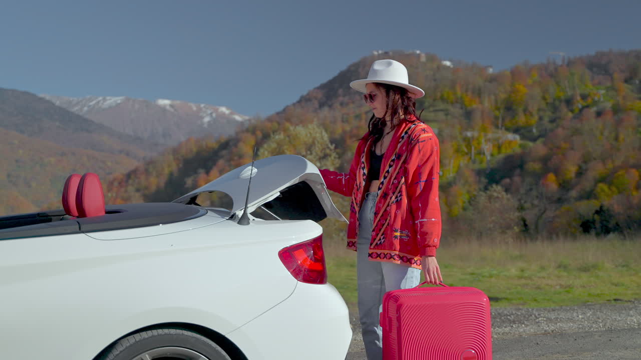 mujer cargando una maleta en un coche convertible en un paisaje panorámico de montaña