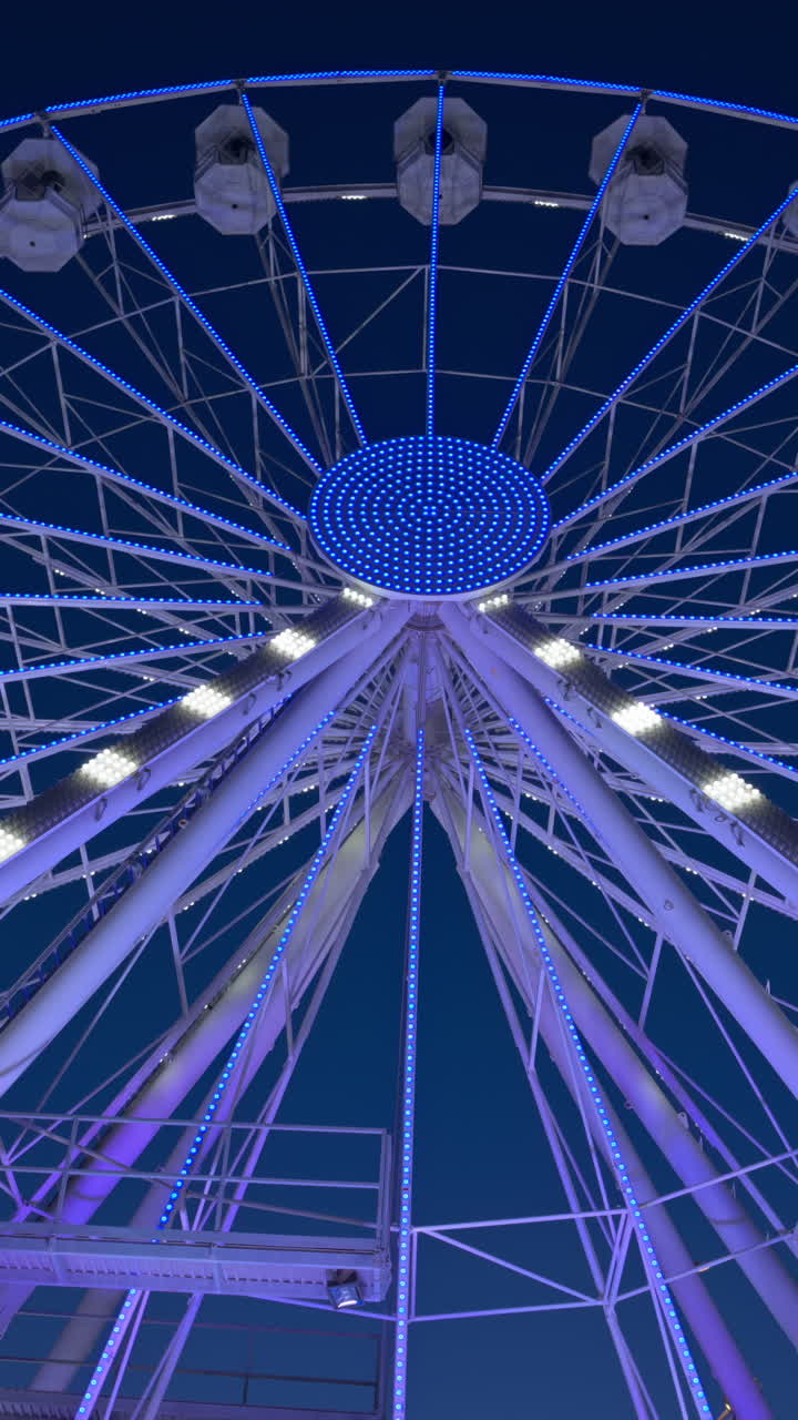 View of a white ferris wheel illuminated in the evening with the blue sky on the background. Vertical