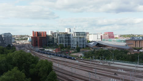 Aerial-view-of-train-unit-leaving-train-station-on-multi-track-railway-line.-Modern-apartment-buildings-around-track.-London,-UK