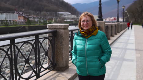 woman walking along a river in a city with mountains