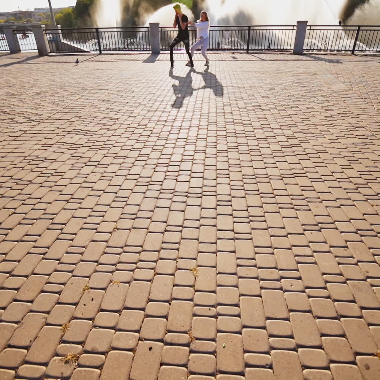 Modern dancers are dancing in the street. Urban lifestyle. Hip-hop generation. Boy's and girl's emotional moves on the video. Paving stones and young dacing couple at fontain background. Aerial view. Young beauty dances behind handsome boy.