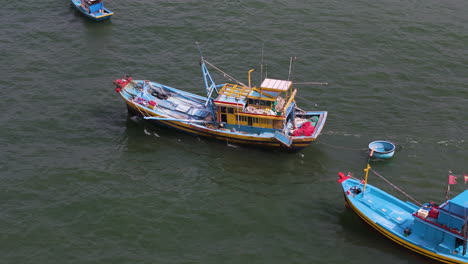 vibrant yellow and blue fishing boat in vietnam drags round circular boat behind, aerial tracking