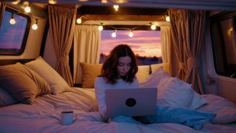woman working on laptop in a cozy camper van at sunset
