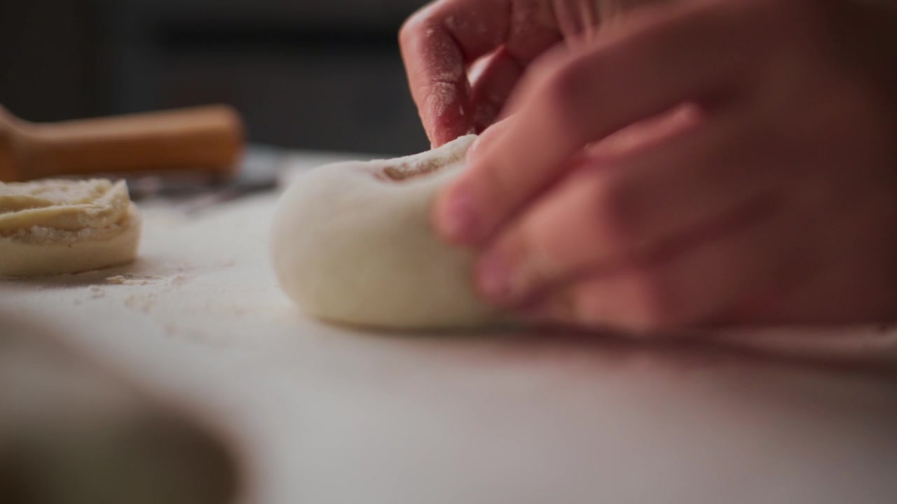 Hands gently roll dough on a floured surface. Focus on careful, precise motion. Ideal for food preparation or cooking tutorials. Evokes calm, methodical energy. Can be used for baking, pastry