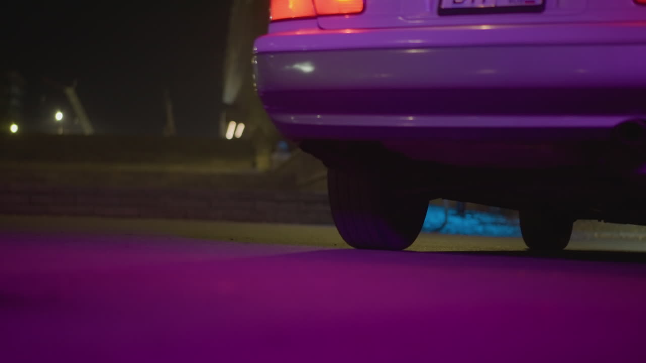 Calle nocturna con luces de neón con primer plano trasero de un coche, pavimento púrpura brillante, luz trasera iluminada, ligera neblina de escape, avenida vacía, taxista esperando a altas horas de la noche, ambiente cinematográfico melancólico