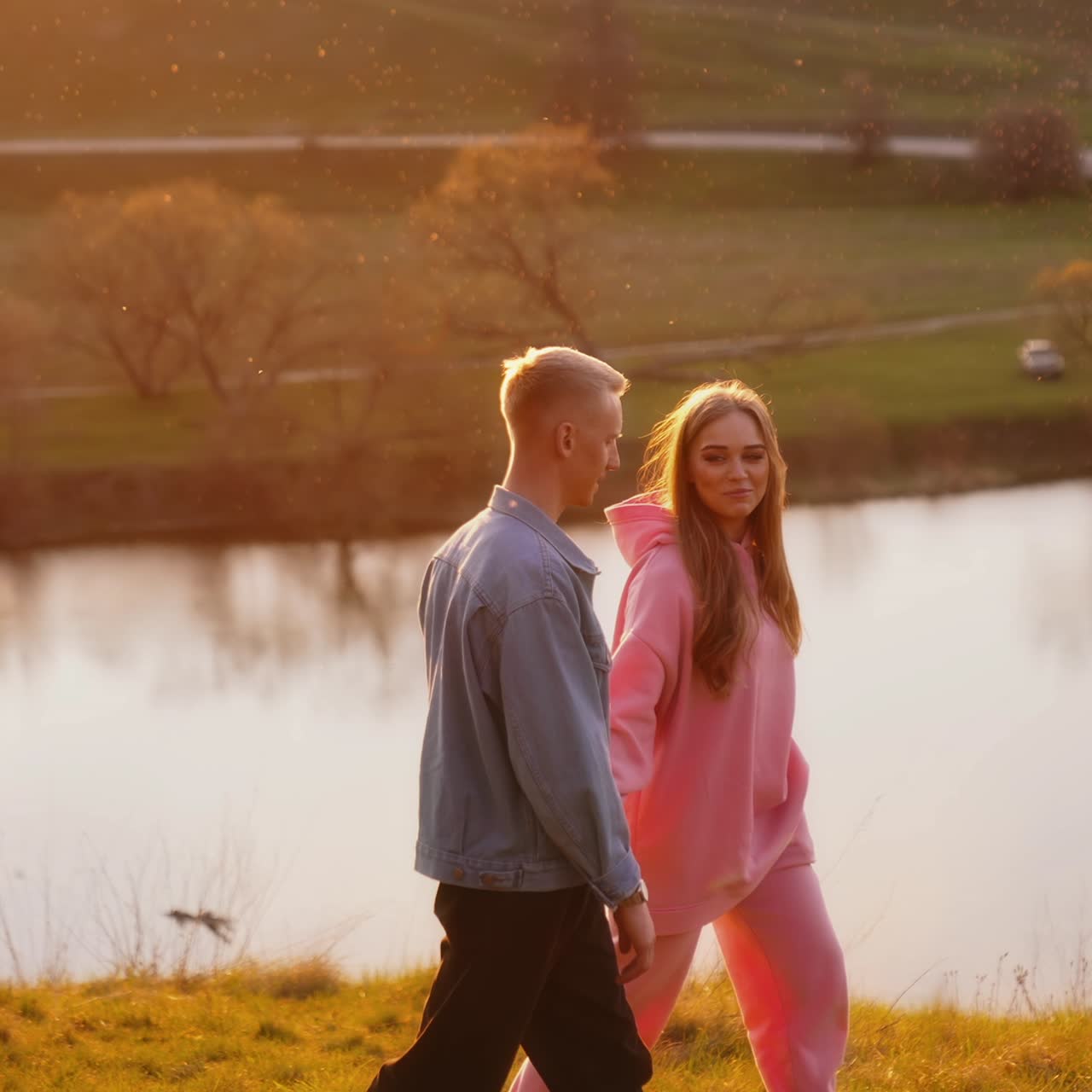 Young man and woman spending time together outdoors. Couple holding hands are walking near the river with happiness