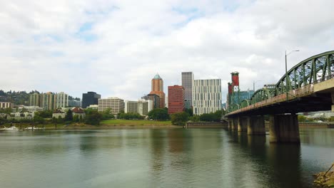 4K-Boom-Up-Enthüllung-Hinter-Einem-Busch-Zur-Hawthorne-Brücke,-Die-Den-Willamette-Fluss-In-Richtung-Downtown-Portland-überquert,-Oregon-Skyline-Mit-Meist-Bewölktem-Himmel