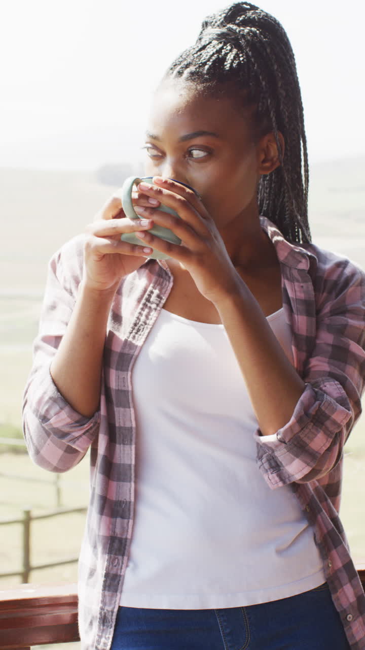 Vertical video of african american woman drinking coffee in log cabin