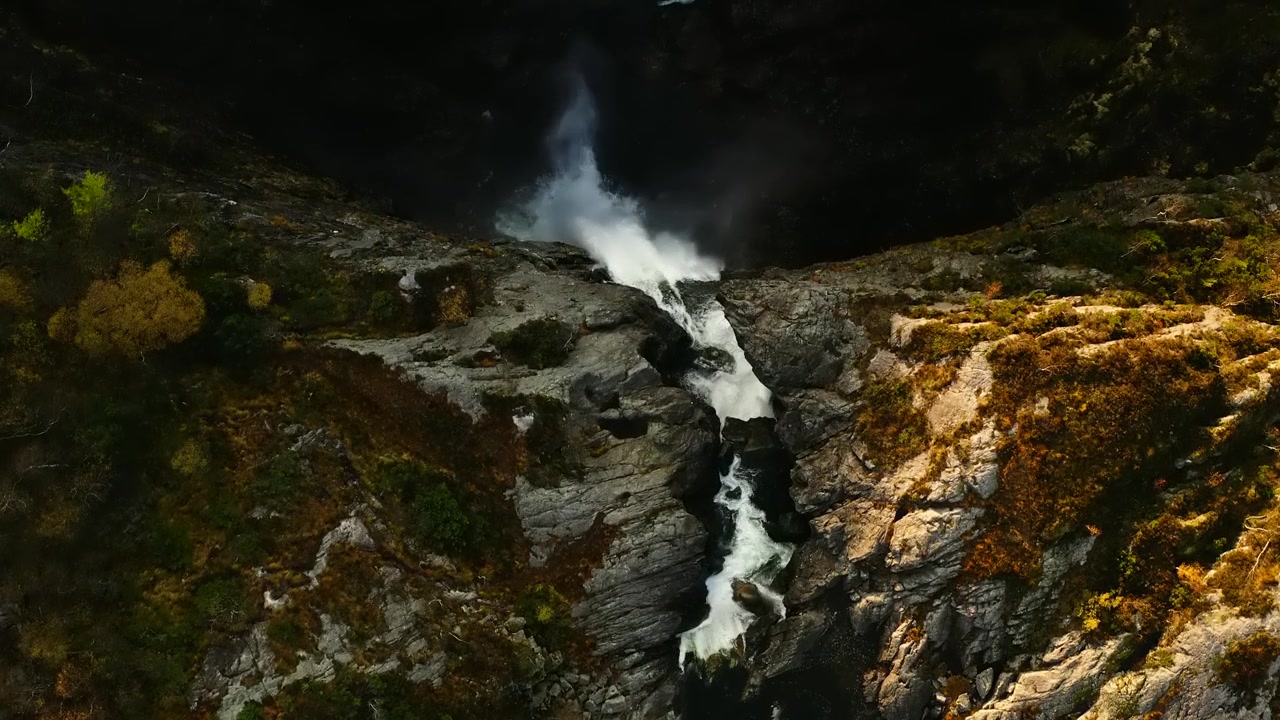 Vista aérea de una cascada de montaña con niebla y terreno rocoso.