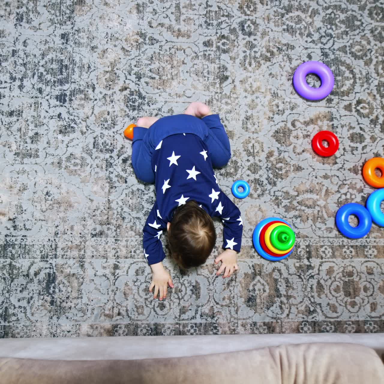 Baby boy trying to reach under the sofa. Kid plays on the floor indoors. Top view perspective