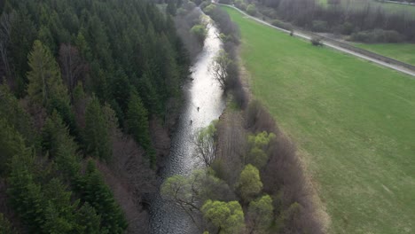 Aerial-descending-shot-of-fishermen-wading-through-the-river-at-the-bottom-of-the-Lower-Tatras-mountains,-river-hron