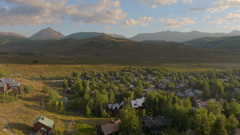 aerial push over houses in crested butte, colorado and towards the rocky mountains on the horizon on a beautiful sunny morning