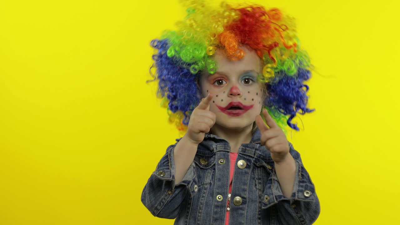 una niña payasa con una peluca arco iris haciendo caras tontas. divirtiéndose, sonriendo, bailando. halloween