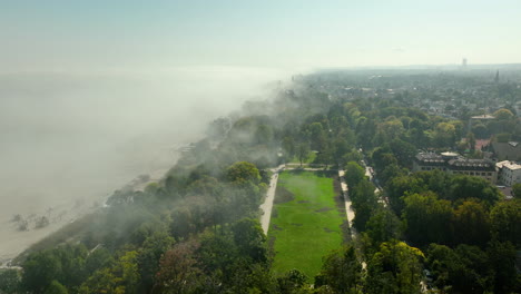 Aerial shot of Sopot beach and coastal park covered in fog, with only parts of the city visible