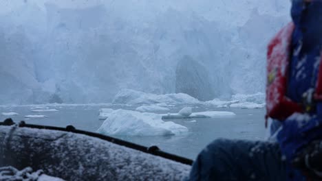 Polar-Expedition,-Boat-Sailing-Under-Glacier-by-Floating-Ice-on-Cold-Snowy-Day,-Slow-Motion