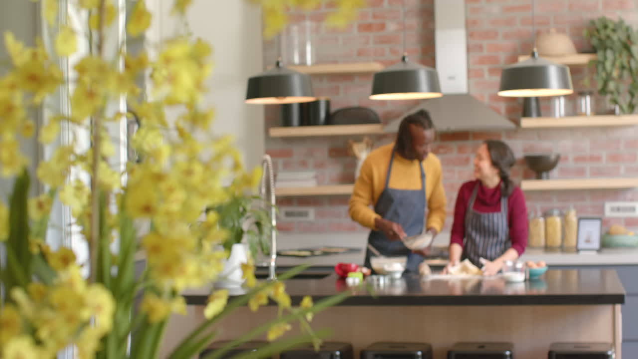 Coppia felice e multietnica con grembiuli che cucina in cucina, spazio per il testo, slow motion
