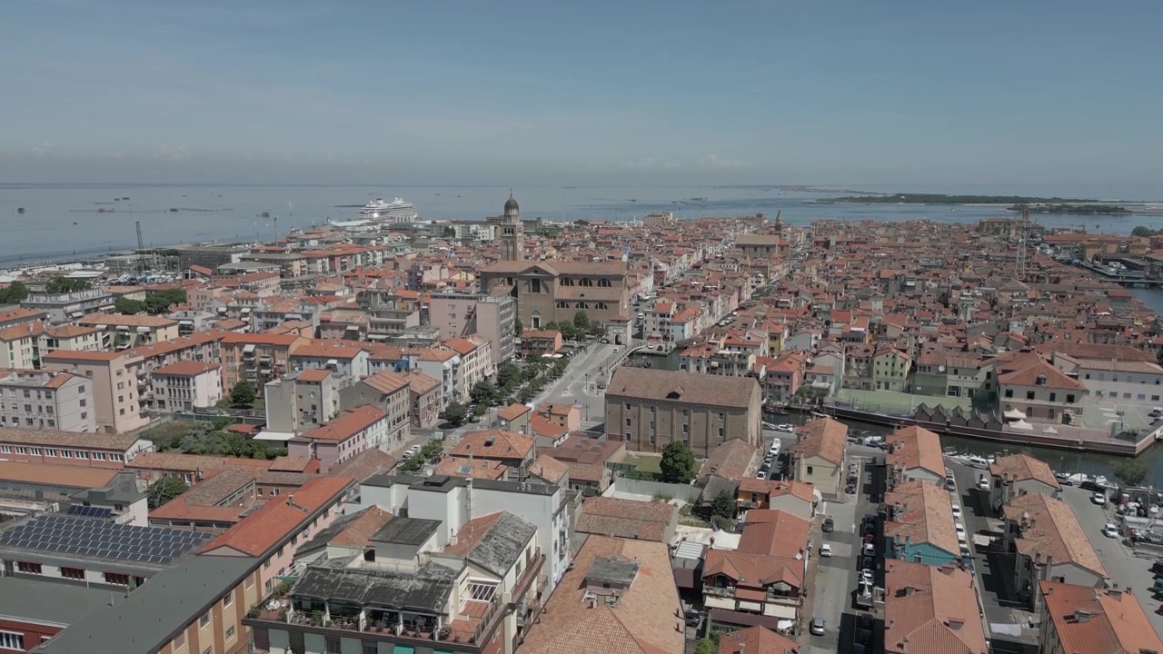 Ripresa aerea con drone in ascesa di Chioggia, Italia, circondata dall'acqua in una giornata estiva.