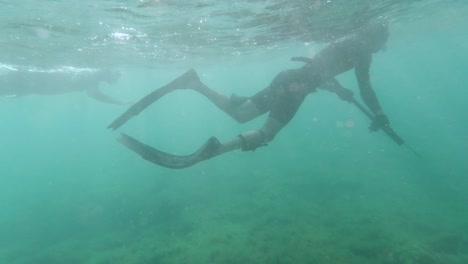 spearfishers snorkeling in shallow water while one points at a direction in the mediterranean sea
