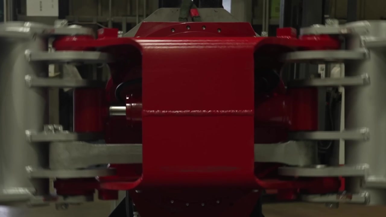 Close up of a red painted grapple body with silver steel arms swinging as the attachment rotates inside a workshop