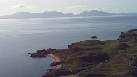 Aerial-view-circling-above-idyllic-Ynys-Llanddwyn-island-with-hazy-Snowdonia-mountain-range-across-shimmering-Irish-sea-at-sunrise