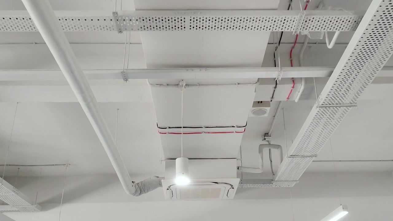 Veduta dal basso verso l'alto del soffitto di un moderno ufficio aziendale con un'unità di climatizzazione a cassetta, condotti di ventilazione e impianti. Ideale per HVAC, interni commerciali e progettazione di spazi di lavoro.