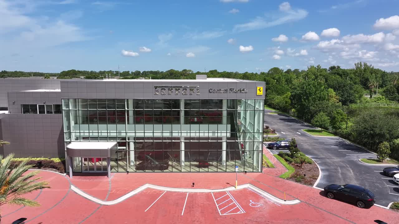 Aerial approaching shot of Ferrari Car Dealership in Central Florida. Historic cars parking inside. Glass facade of building.