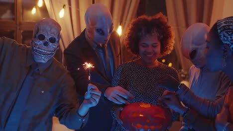 friends lighting sparklers with jack-o-lantern at halloween party